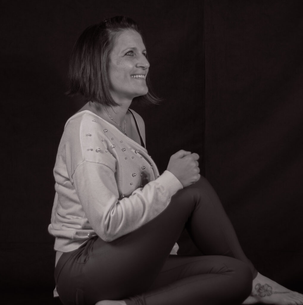 Portrait en noir et blanc de Mélissa Carbone, photographe à Grasse, assise et souriante dans son studio.